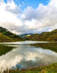 Serene mountain lake reflects a cloudy sky. Lush green hills surround a calm body of water