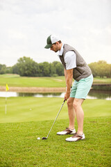 Fototapeta premium Man, sport or playing golf with club on grass field for hole shot, round or outdoor match on course. Active, male person or golfer getting ready to swing with stick for score, point or game on pitch