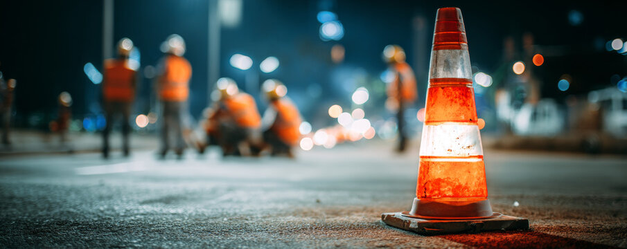 Traffic cone with illuminated light on urban street at night, safety barrier for road work and construction zones