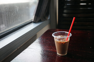 plastic cup of vietnamese iced milk coffee with red straw served on wooden table next to window inside vietnam railways train carriage during travel journey