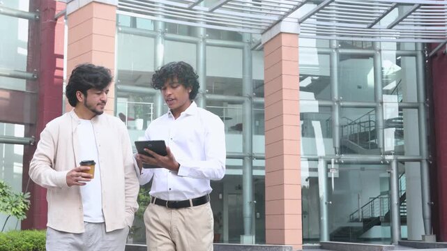 Young indian men entrepreneurs or business professionals discussing work while walking, sharing ideas and do project using digital tablet outdoor office building, teamwork and corporate lifestyle. 4k