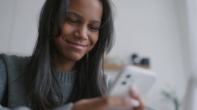 Cheerful african american woman using smartphone at home, be online, portrait. Black lady smiling when looking at screen of mobile phone, reading messages and watching memes in social networking