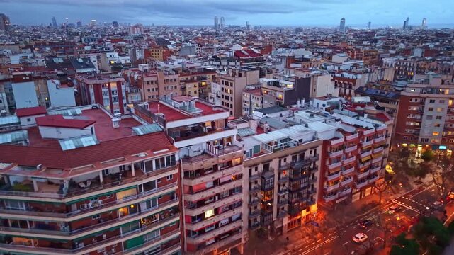 Aerial drone footage flying over rooftops and illuminated streets of La Nova Esquerra de l'Eixample neighborhood at dusk, Spain