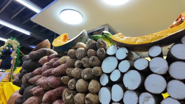 Travelling shot piles of fresh tubers in a bustling local market. cassava, pumpkin, sweet potato, taro