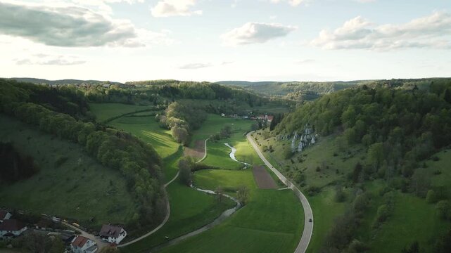 Smooth 4K UHD drone push-in flying forward down the Gro&szlig;e Lautertal, tracking the meandering Gro&szlig;e Lauter through green meadows, past a country road and limestone slopes of the Swabian Alb.
