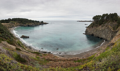 Naklejka premium Coastal Bay Cove With Cliffs, Turquoise Water, and Overcast Sky
