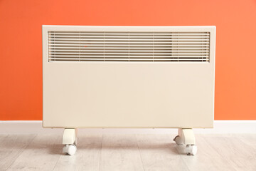 Modern electric convector heater on floor near orange wall in room