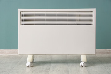 Modern electric convector heater on floor near turquoise wall in room