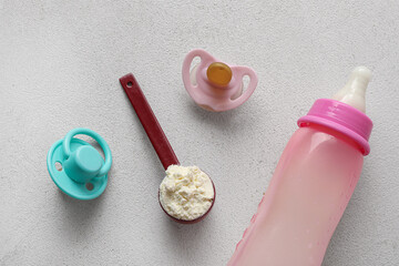 Scoop of powdered baby milk formula with bottle and pacifiers on grunge white background