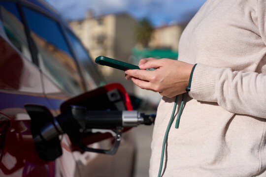 Woman using smartphone refilling environmentally friendly vehicle with alternative fuel