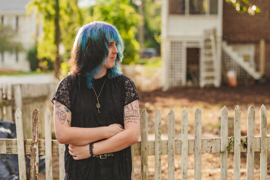 Transwoman looking away leaning on a white picket fence wearing black