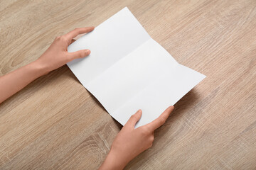 Obraz premium Female hands with blank brochure on wooden background, closeup