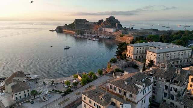 Aerial view of the Old Fortress of Corfu and the harbor at sunrise. Peaceful morning scene with boats docked, calm water, and historic Venetian architecture