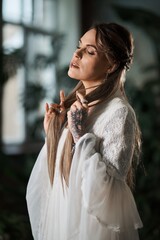 Elegant woman with long blonde hair and intricate lace dress poses thoughtfully indoors