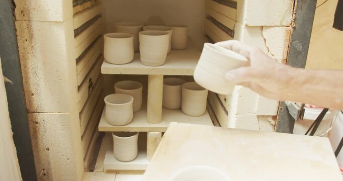 Senior caucasian man wearing apron firing pots in kiln at pottery workshop