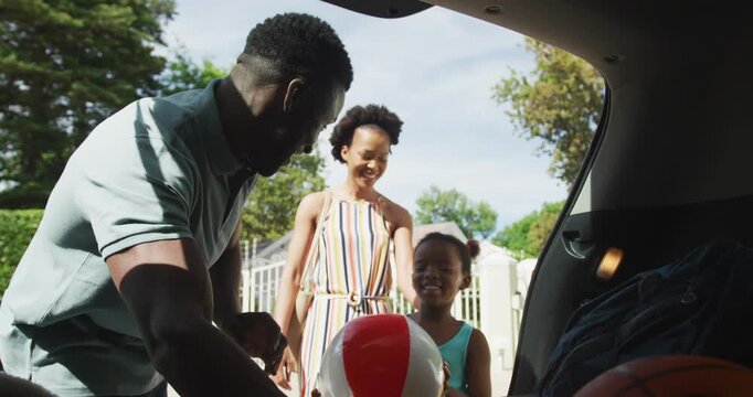 Happy african american family packing car with beach balls on holiday