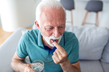 Taking Medication and Pills. Healthcare and Treatment, People with pharmacy concept, Healthcare and Medicine concept. Elderly man sitting on sofa and putting pill in mouth with glass of water.