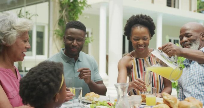 Happy african american family drinking juice and having breakfast in garden