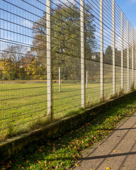 Fototapeta premium Fenced soccer field near a walking path on a clear autumn day with fallen leaves
