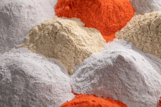 An angled, close-up photo shows three distinct mounds of high-quality nanostructured powder paint in bold orange, bright white, and pale beige.