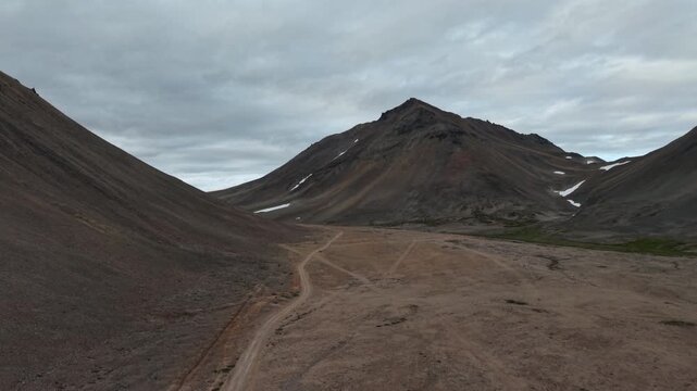 Aerial view of Russia, Chukotka, Provideniya mountain pass and winding dirt road. Slow lateral glide right reveals the valley floor under overcast daylight. Epic wilderness destination for travel
