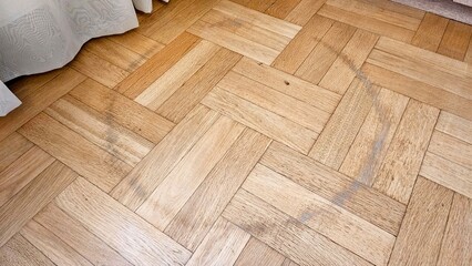 Light-colored circular water stains on herringbone oak parquet flooring corner near white curtain and carpet edge, household maintenance detail.