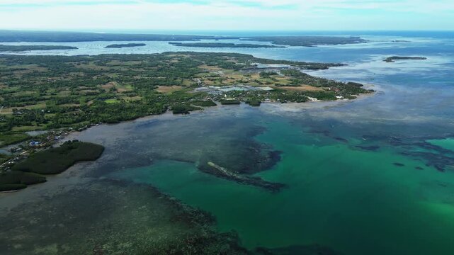 Wide aerial showing Tondol island fully in frame with palm trees, bright white sand, and calm tropical water.