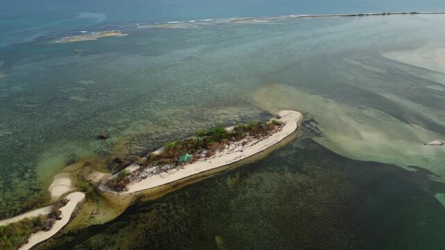Aerial focusing on white sand island edge with palm trees and shallow turquoise water at Tondol Beach.