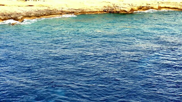 Deep blue Mediterranean ripples dance under the bright summer sun near the coast of Gozo and Comino Malta as the high angle camera captures the turquoise subsurface glow in the crystal clear water