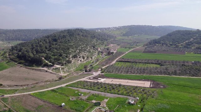 Aerial drone shot of Nahal Zippori (Tzippori Stream) in northern Israel, showing the green valley, winding dirt roads, olive trees, and the historic Monks Mill (Tahanat HaNezirim) nestled along the st