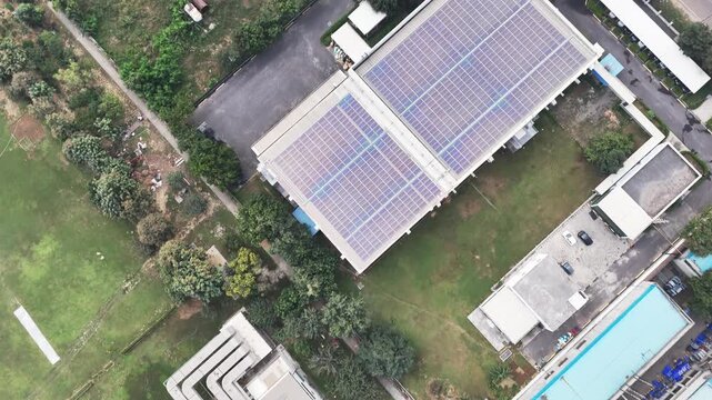 Drone shot of factory rooftops lined with solar panels and service roads below, capturing sustainable industrial infrastructure in Greater Noida under a thin layer of atmospheric smog.