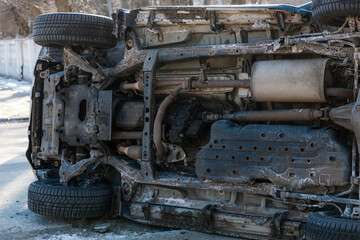 Fototapeta premium A detailed medium shot of the undercarriage and front suspension of an overturned SUV after a road accident. The image shows the complex mechanical components, chassis, and dirty body panels of the ve