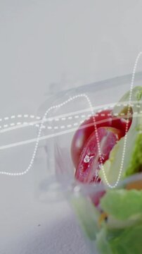 Vertical video: Waveform moving, frame panning, halved tomato and greens in clamshell showing fresh