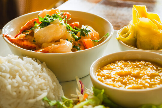 Traditional Creole meal from Seychelles featuring succulent grilled prawns in a rich garlic butter sauce, accompanied by flavorful lentils, a refreshing mango salad, and aromatic basmati rice.