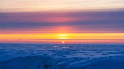 Fototapeta premium Serene sunset over a vast icy landscape, painting the sky with warm hues of orange, pink, and purple