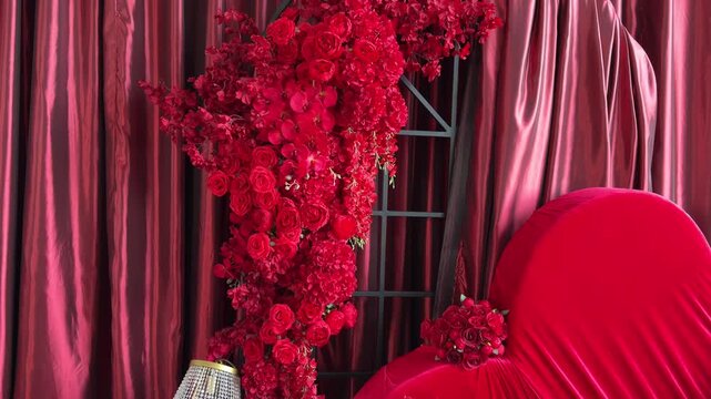 Zoom out from red roses, orchids arrangement and large velvet heart. Luxurious studio interior with crimson silk curtains. Elegant romantic backdrop for Valentines Day or wedding photography.