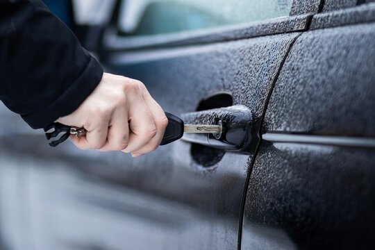 Close-up of a hand holding a key near a frozen lock on a black car, winter cold concept, automotive trouble, icy weather, security and access.