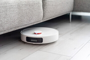 White circular robot vacuum cleaner cleaning under the sofa