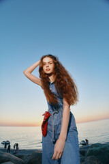 Lifestyle woman in modern boho-western denim street style posing by the seaside during golden hour with film color tones and relaxed natural expression.