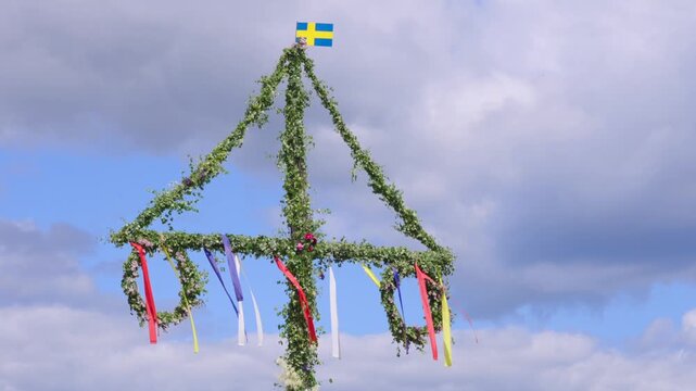 Midsummer pole or maypole on sunny day in Sweden. decorated with swedish flag. Moving slowly in light wind