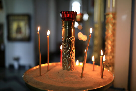 Many lit church candles in sandbox with religious icon frame in the background