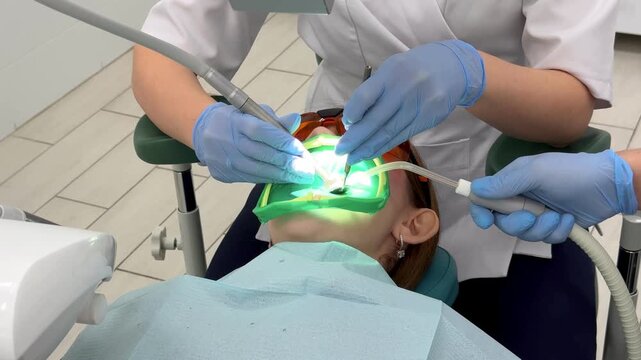 A dentist performs a dental filling procedure on a young girl with high-precision instruments in a modern clinic.