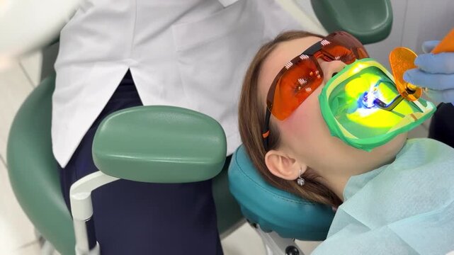 Applying a composite filling to a tooth. Young woman in a dental clinic. Female dentist with assistant treats dental caries in patient's mouth