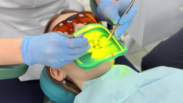 Applying a composite filling to a tooth. Young woman in a dental clinic. Female dentist with assistant treats dental caries in patient's mouth