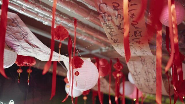 Red and white paper lanterns with calligraphy scrolls and ribbons hanging from a ceiling, swaying gently in the wind during a festive celebration, creating a beautiful and serene cultural display