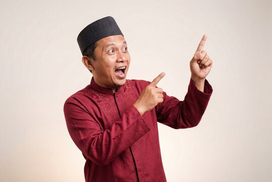 Surprised asian man wearing a kopiah points to the left with a wide eyed expression