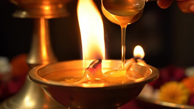Close up of a hand pouring oil into a traditional brass oil lamp with a bright flame and bokeh background