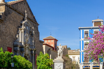 Statue of Carlos V in Plaza de la Universidad Granada Spain with Baroque Church of Santos Justo y Pastor and Pink Judas Tree Flowers Historic University Square Architecture