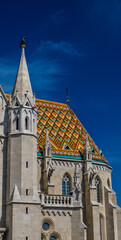 Fototapeta premium The photograph shows a fragment of Matthias Church and the Fisherman's Bastion in Budapest, with its pointed Gothic-style turrets against a blue sky.