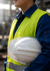 Fototapeta premium Industrial Safety Worker: Close up of engineer in blue uniform and high visibility vest holding white helmet, construction site security, labor protection, factory maintenance and engineering concept